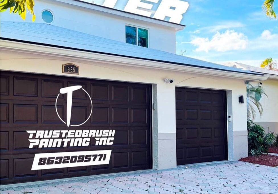 IMG_1997 Garage doors with dark brown paint and a Trusted Brush Painting Inc advertisement, including a logo and contact number, on the left door. A white house is in the background.